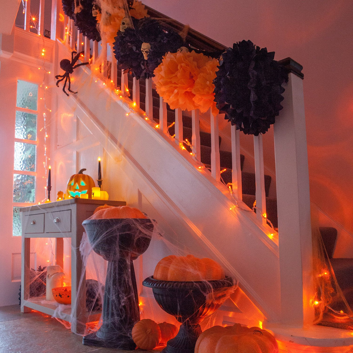 Halloween-Dekoration mit orangener LED-Lichterkette an Treppe mit Kürbissen und Spinnennetz