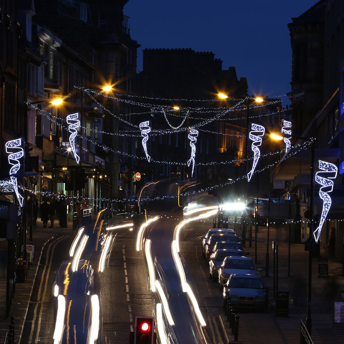 Straßenansicht mit weißen LED-Weihnachtslichtern und Lichtspuren von Fahrzeugen bei Nacht