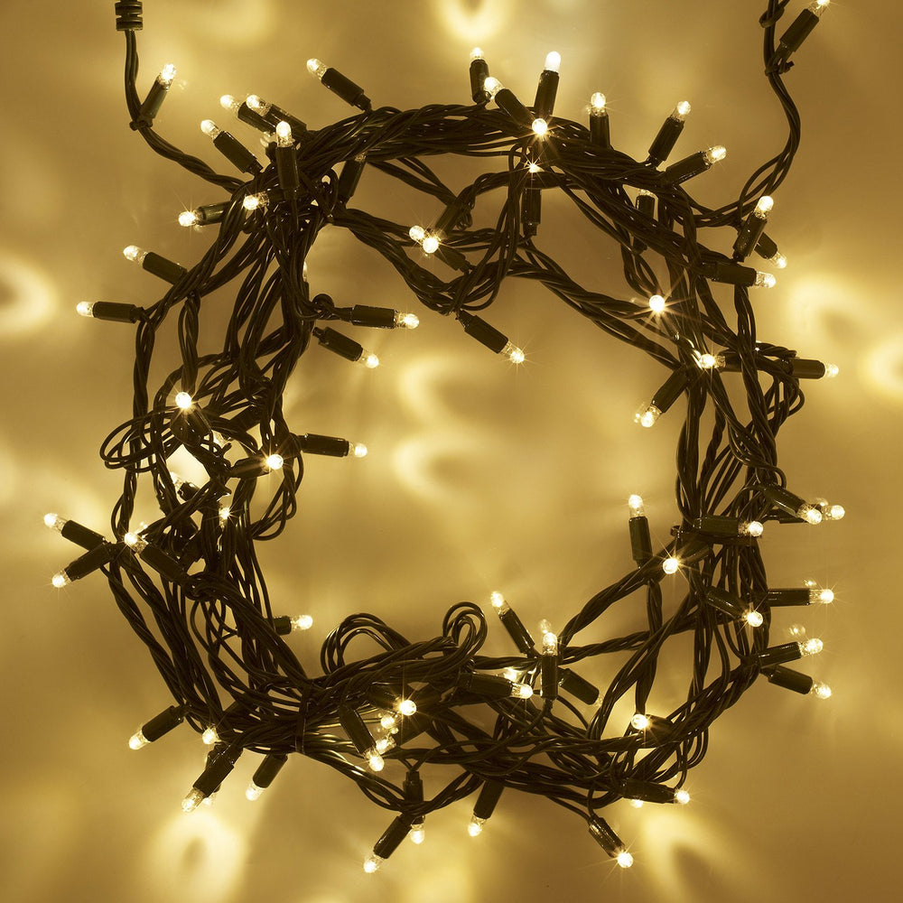Nahaufnahme einer warmweißen LED-Lichterkette mit grünem Kabel, eingeschaltet und auf hellem Hintergrund
