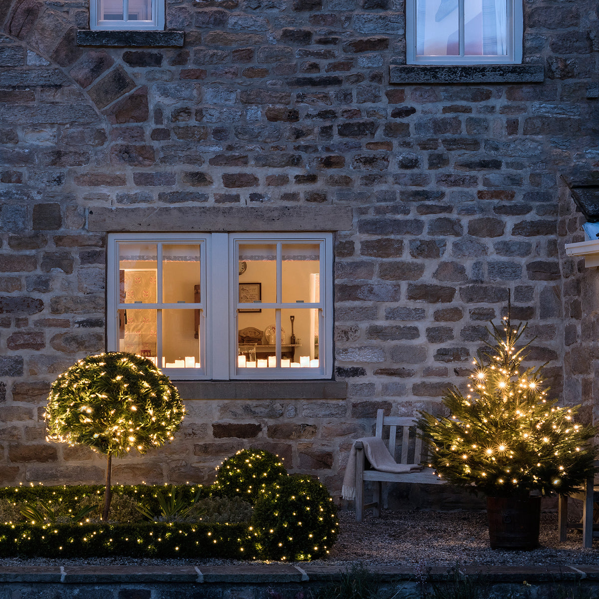Beleuchteter Garten mit warmweißen LED Lichterketten an Büschen und Weihnachtsbaum vor Haus