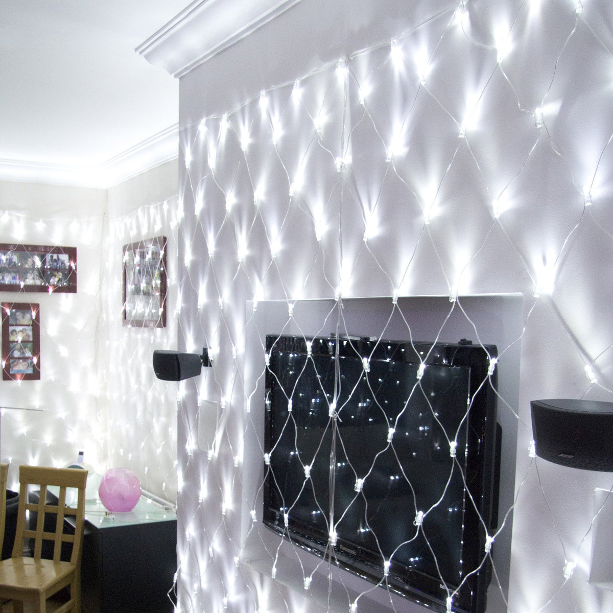 Weißes LED-Lichternetz hängt beleuchtet an Wand über Fernseher und Lautsprecher