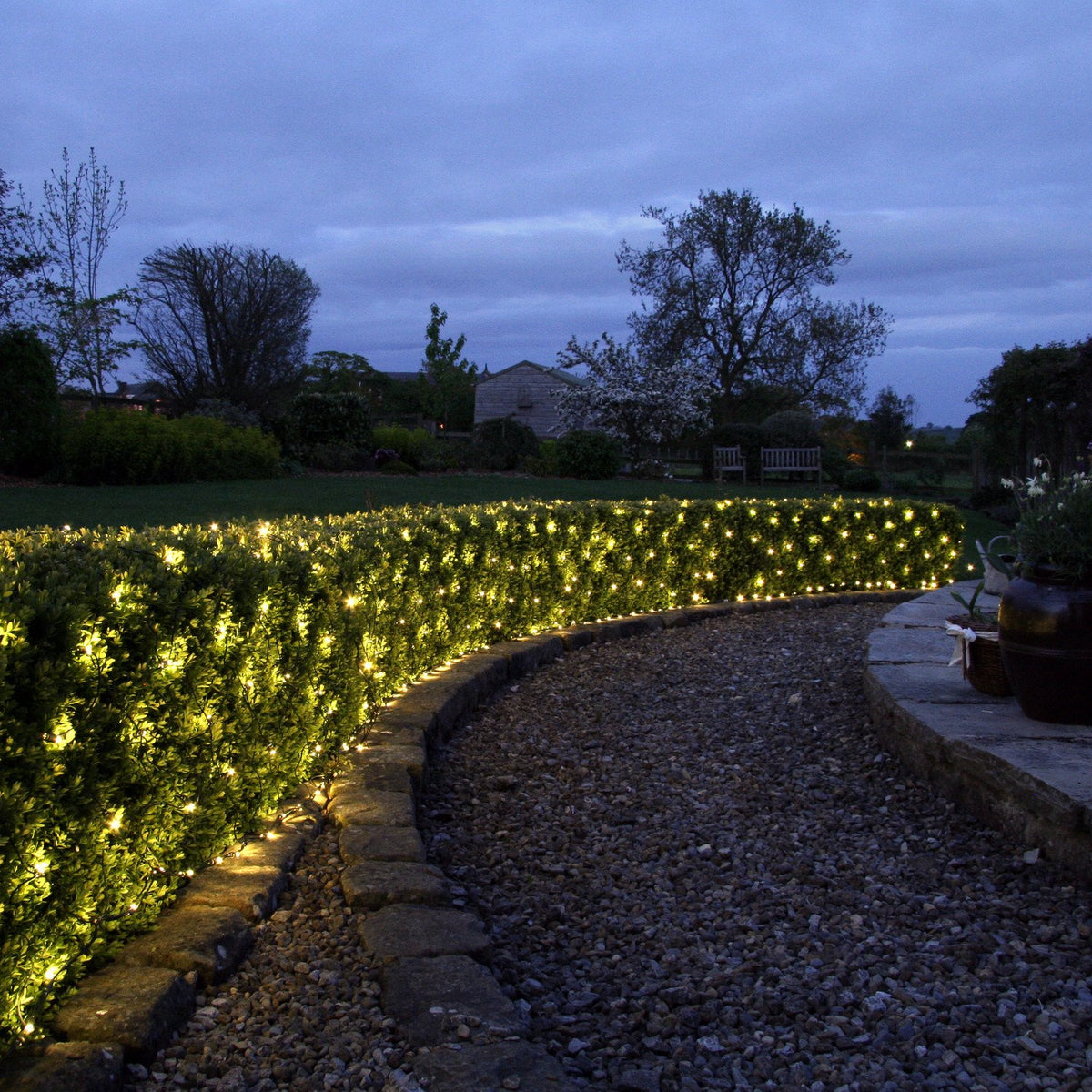 Lichternetz mit warmweißen LEDs dekoriert Hecke entlang eines Gartenwegs