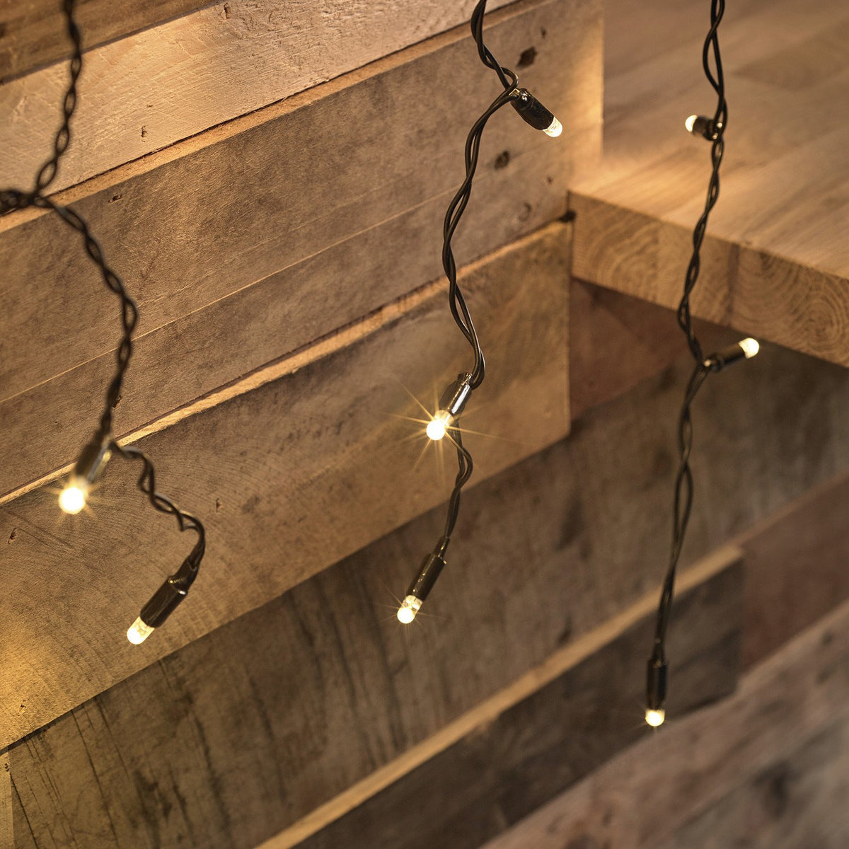 Detailaufnahme von warmweißen LED-Lichtern an schwarzem Kabel vor Holzverkleidung