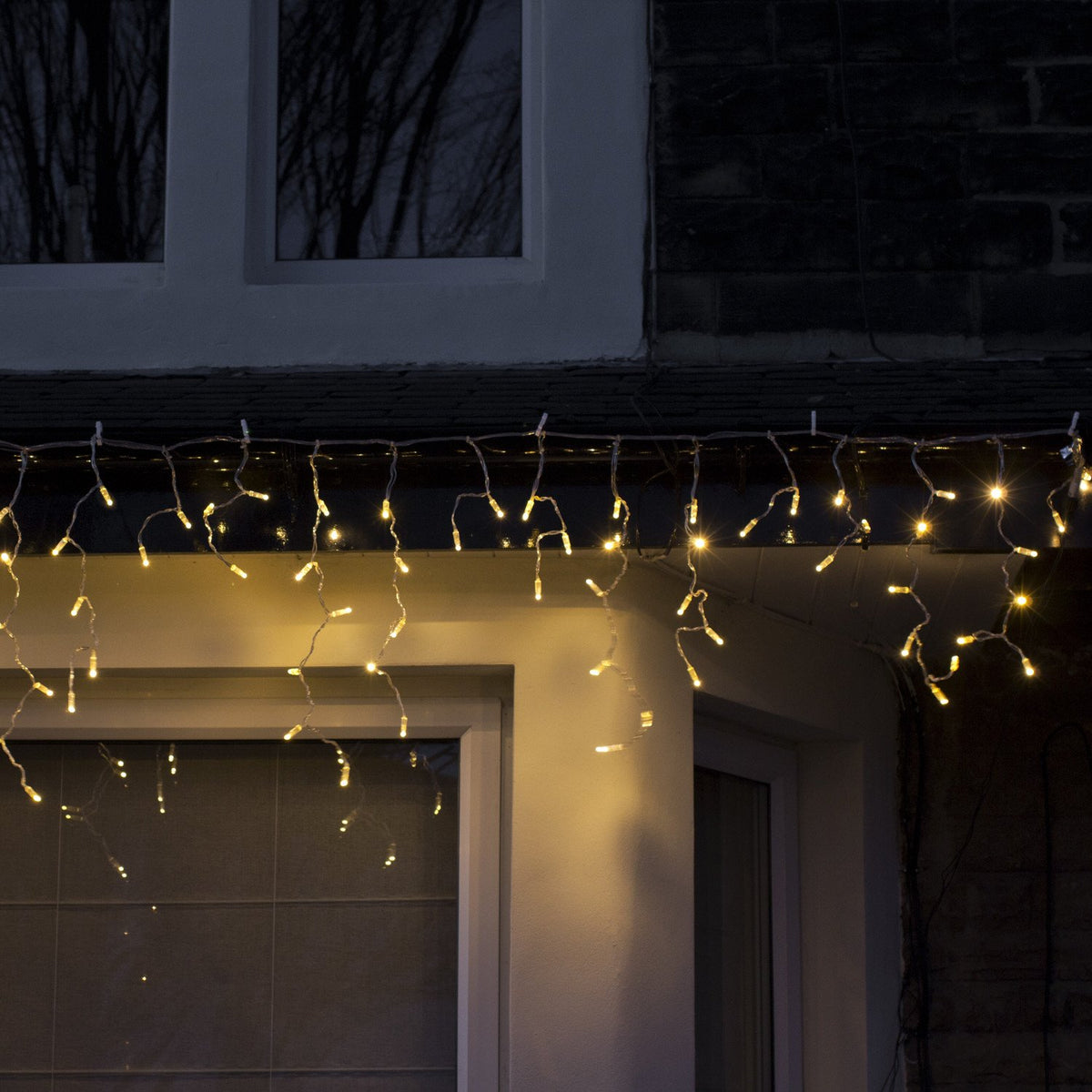 Warmweiße LED Eiszapfen Lichterkette an Dachrinne bei Nacht beleuchtet