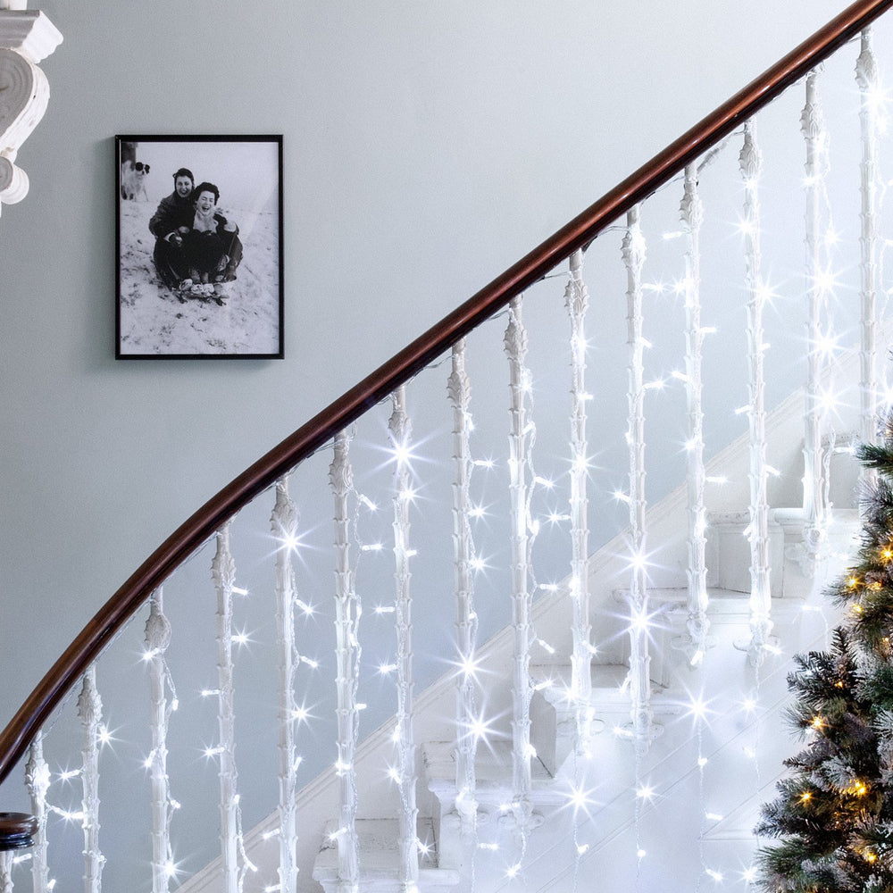 Weißer LED-Lichtervorhang an einem weißen Treppengeländer mit Weihnachtsbaum im Raum
