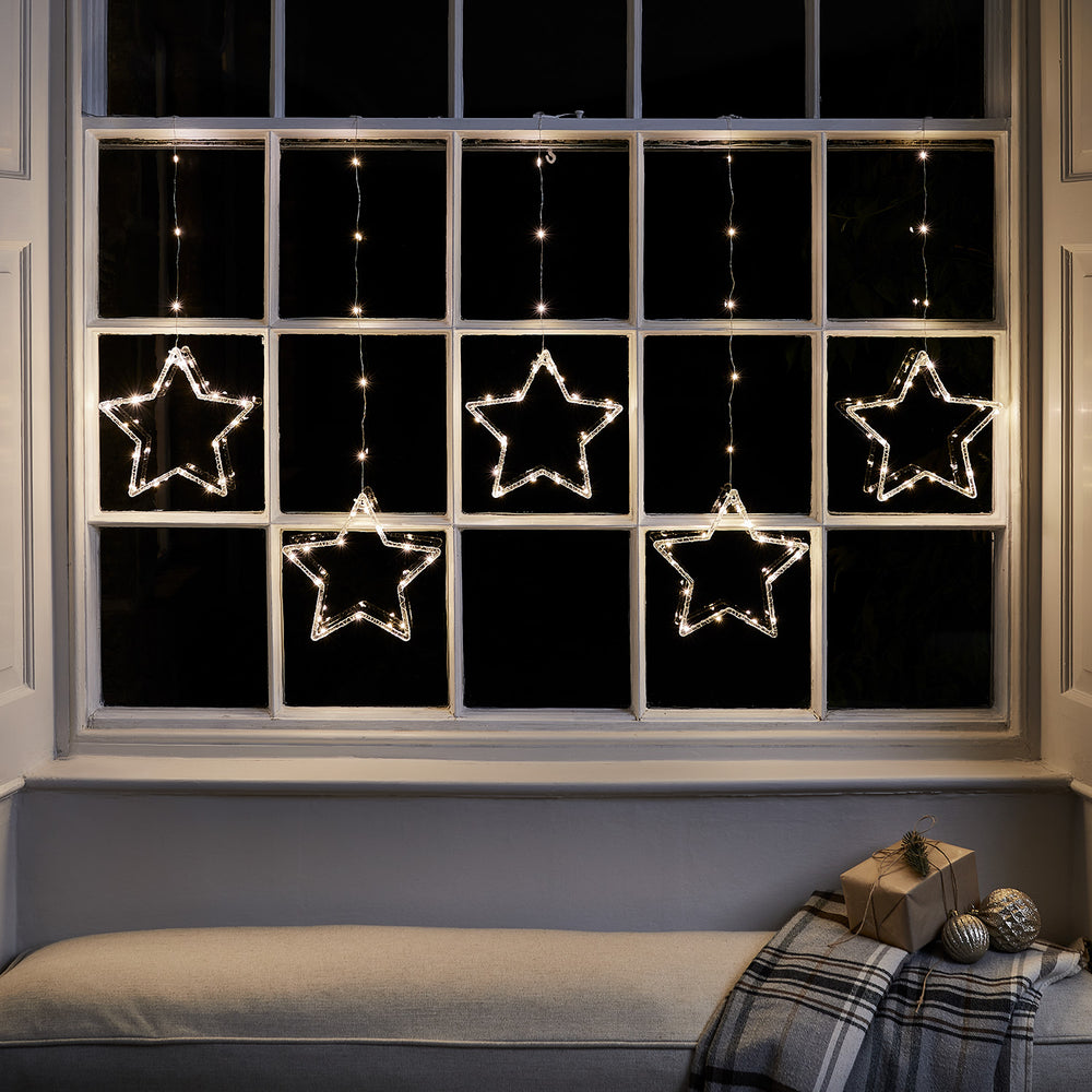 Warmweißer LED-Lichtervorhang mit fünf leuchtenden Sternen an einem Fenster im Dunkeln