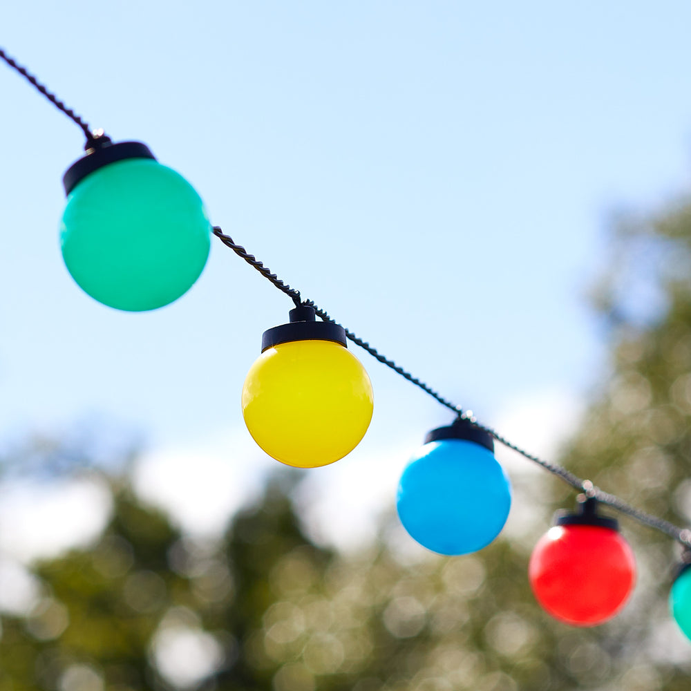 Nahaufnahme bunter Kugellichter in Gelb, Blau, Rot und Grün an Lichterkette im Freien