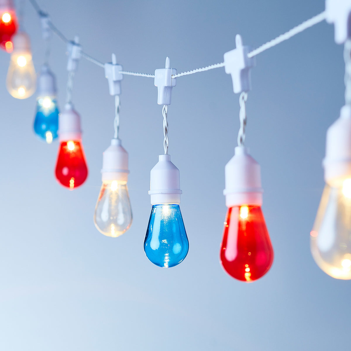 Lichterkette mit rot-weiß-blauen Glühbirnen, aufgehängt an weißen Clips vor blauem Hintergrund