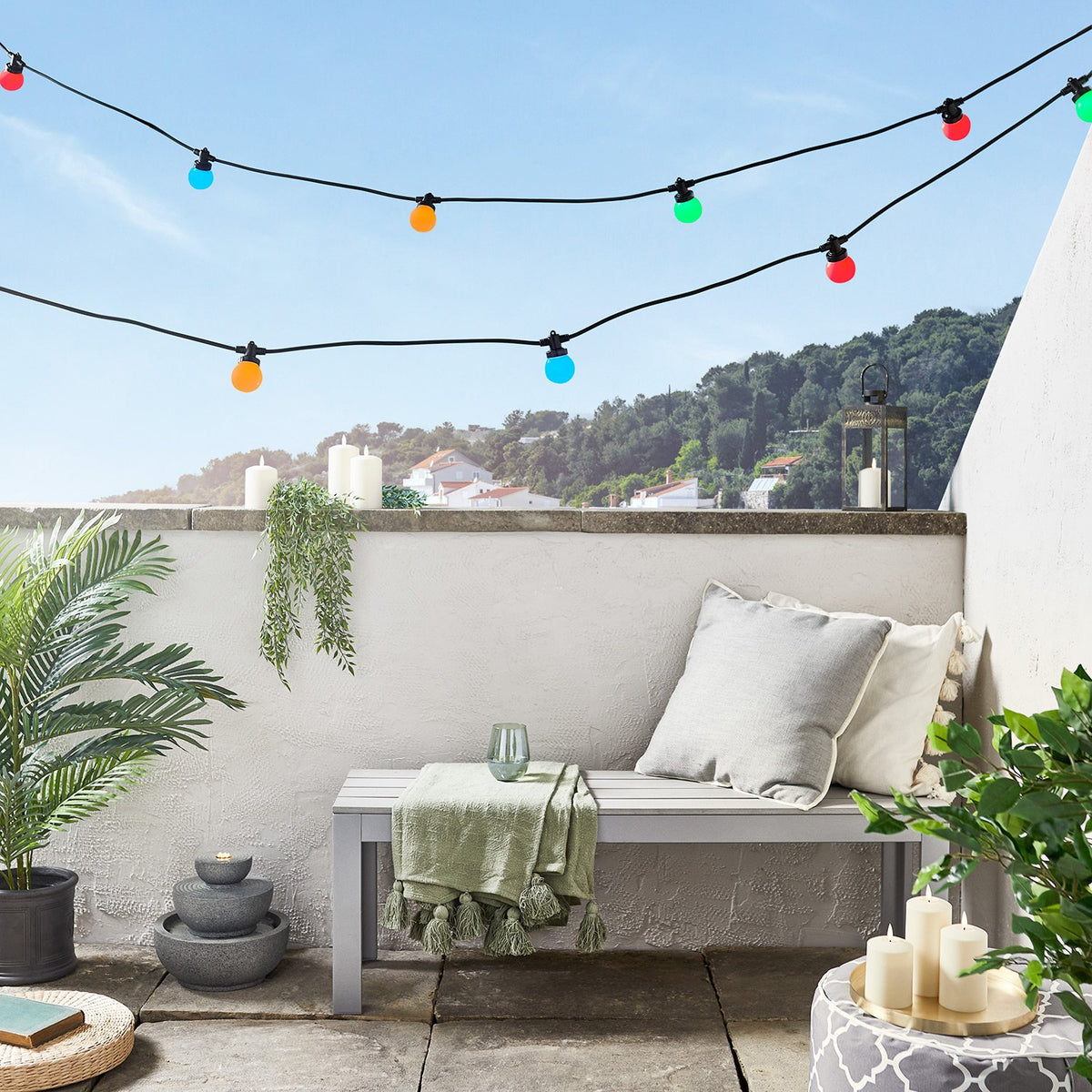 Bunte Lichterkette über Sitzbank auf Balkon mit Pflanzen und Kerzen