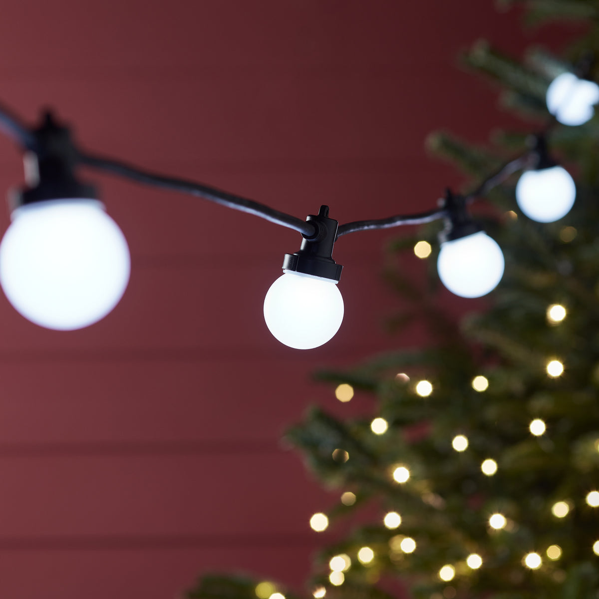 Nahaufnahme weiße LED-Glühbirnen an schwarzem Kabel vor rotem Hintergrund bei Nacht