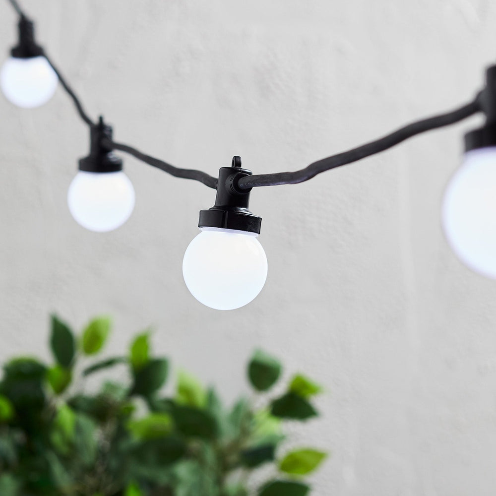 Nahaufnahme weiße LED-Glühbirnen an schwarzem Kabel einer Lichterkette vor weißer Wand