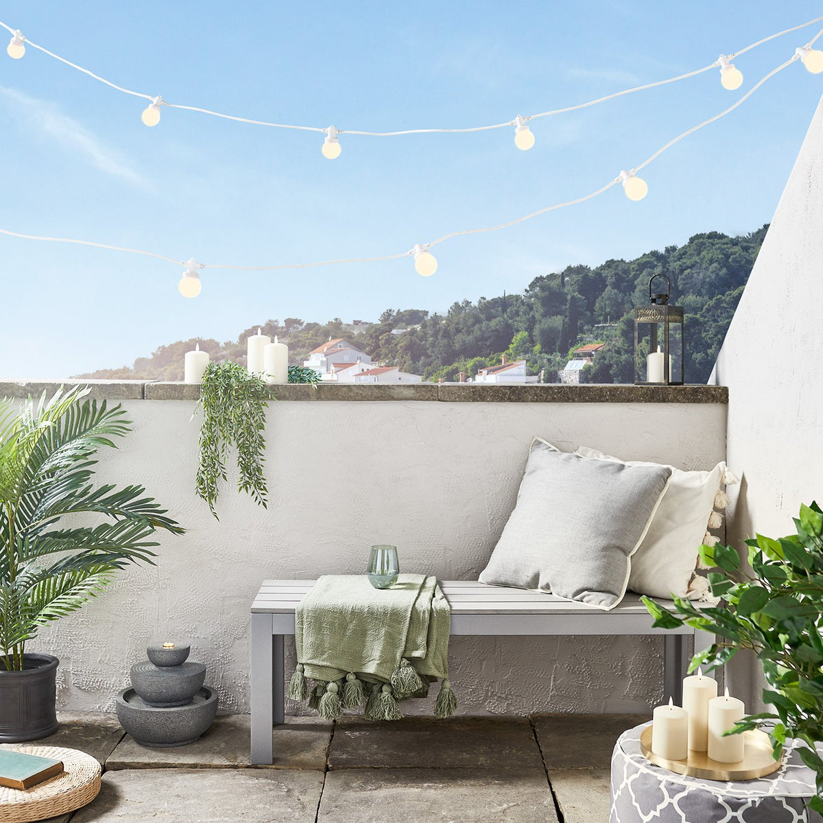 Warme Lichterkette mit weißen Glühbirnen an Balkon mit Sitzbank und Pflanzen