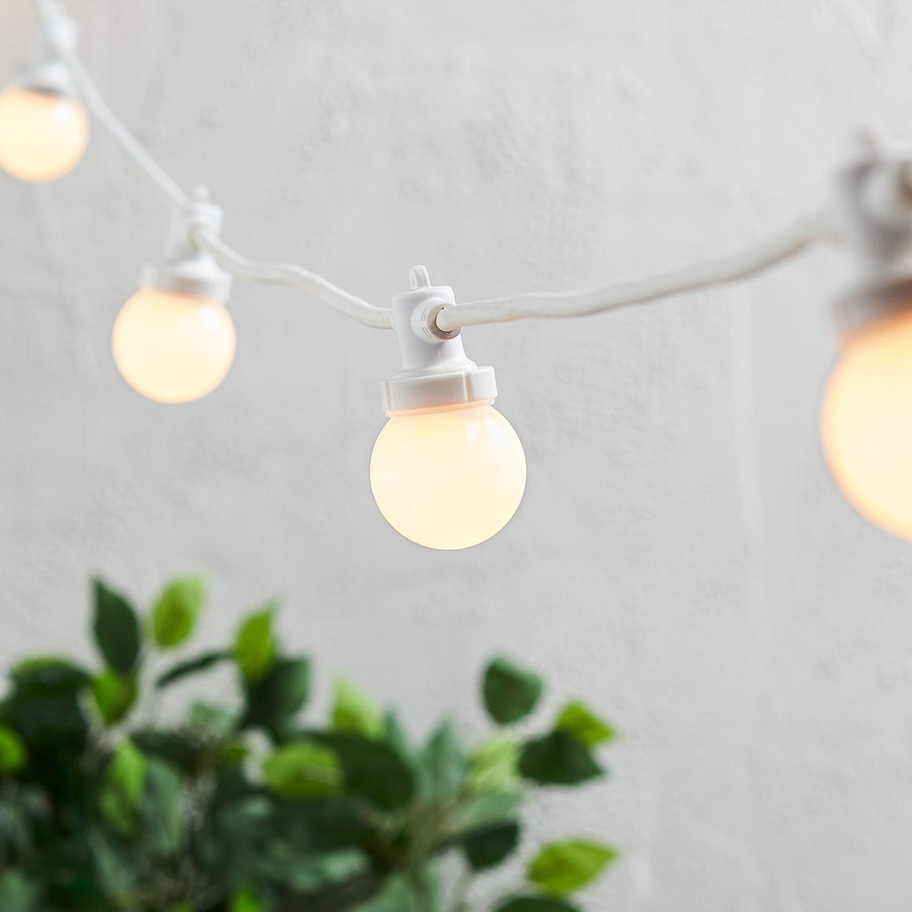 Nahaufnahme einer warmweißen LED-Glühbirne an weißem Kabel vor weißer Wand
