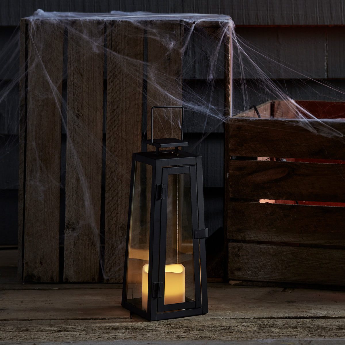 Solar-Gartenlaterne mit LED-Kerze vor Holzkisten mit Spinnweben dekoriert