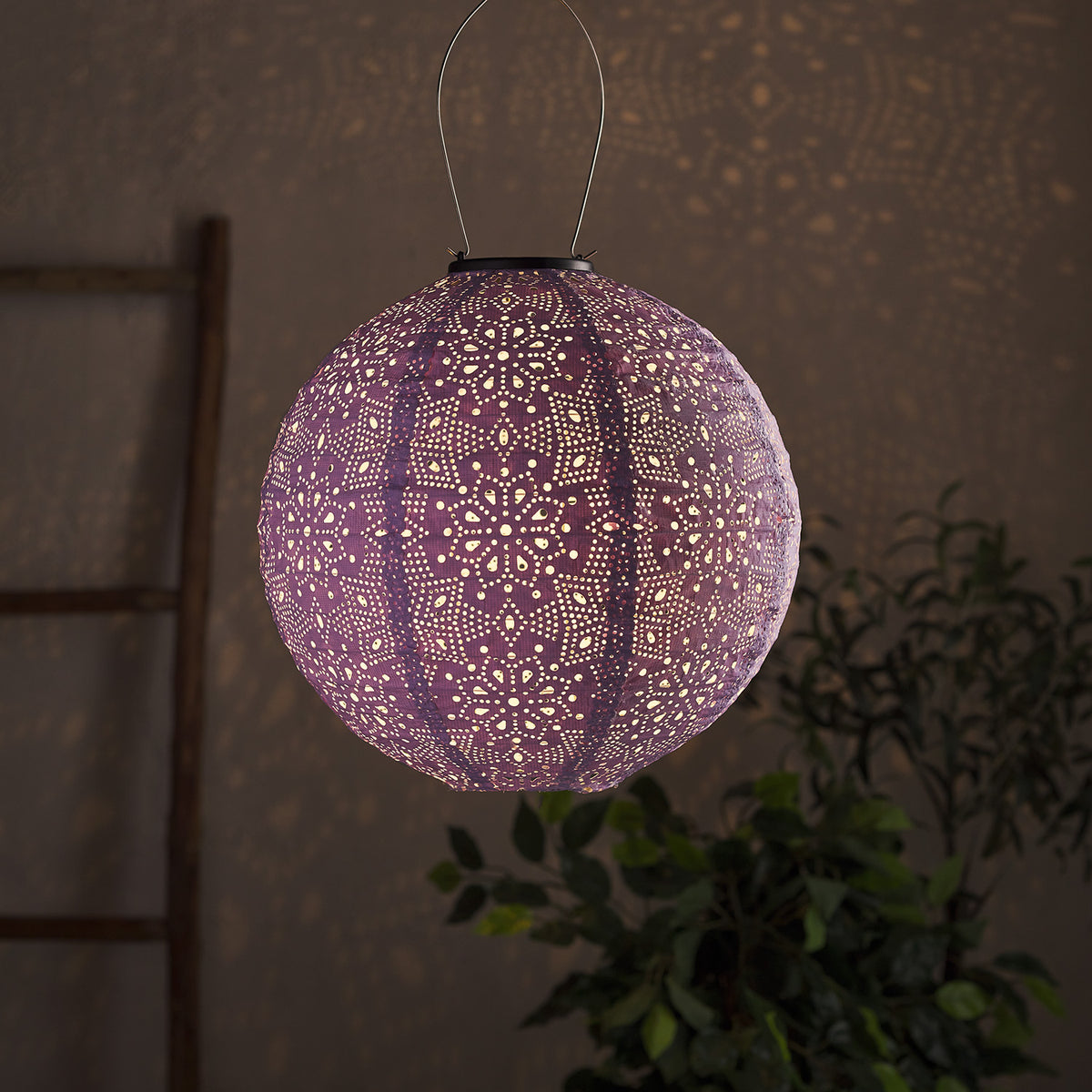 Lila Tyvek Solar Lampion mit Blumenmuster leuchtet und wirft Muster an Wand
