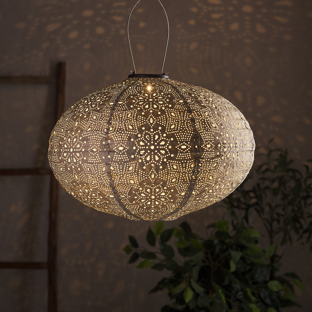 Ovaler silberner Tyvek Solar Lampion mit floralem Muster leuchtet und wirft Muster an Wand