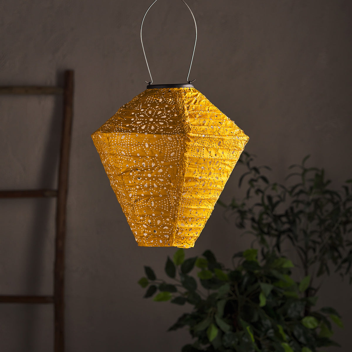 Gelber Tyvek Solar Lampion mit Muster hängt unbeleuchtet vor dunklem Hintergrund