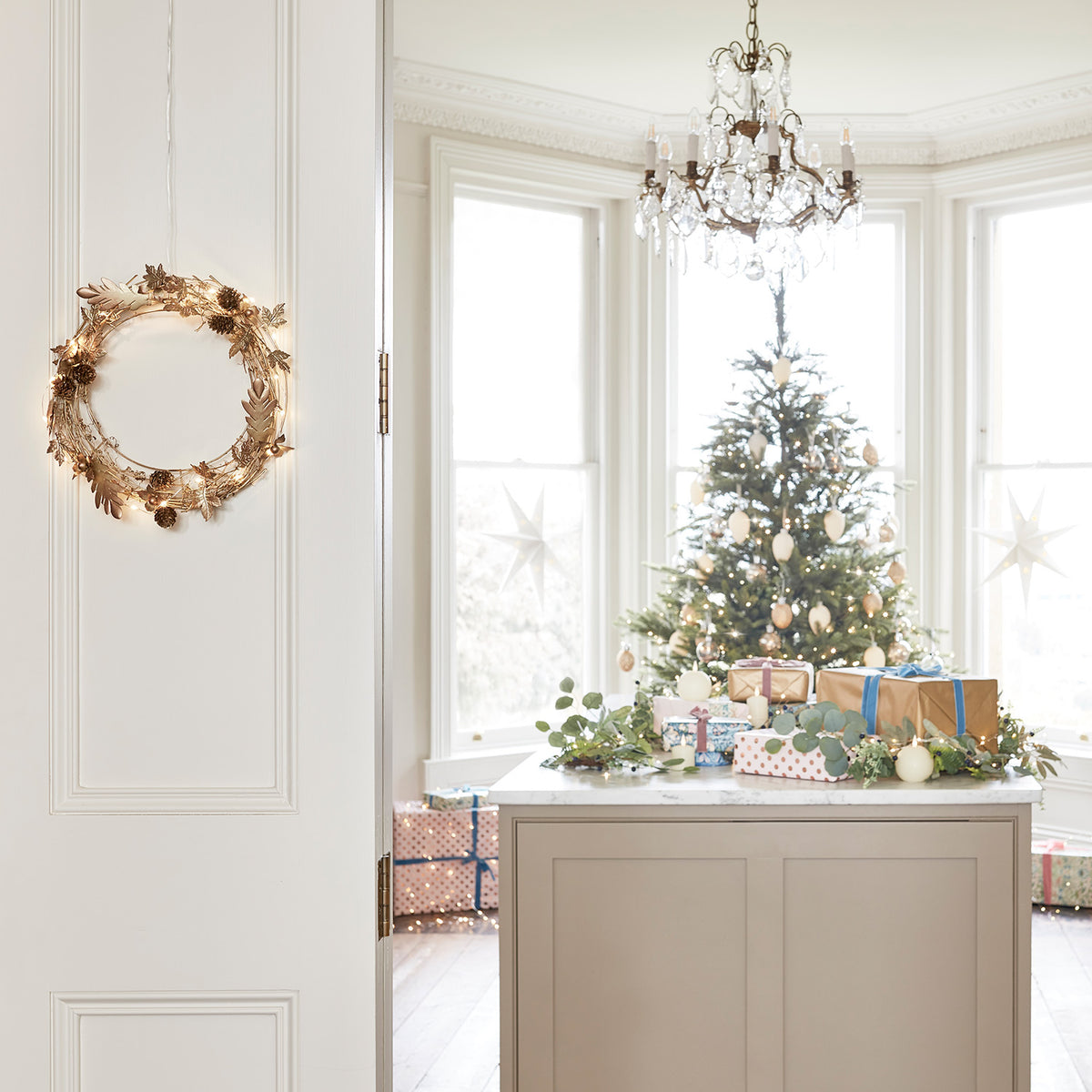 Goldener Weihnachtskranz mit Lichterkette an Türrahmen vor festlich dekoriertem Raum