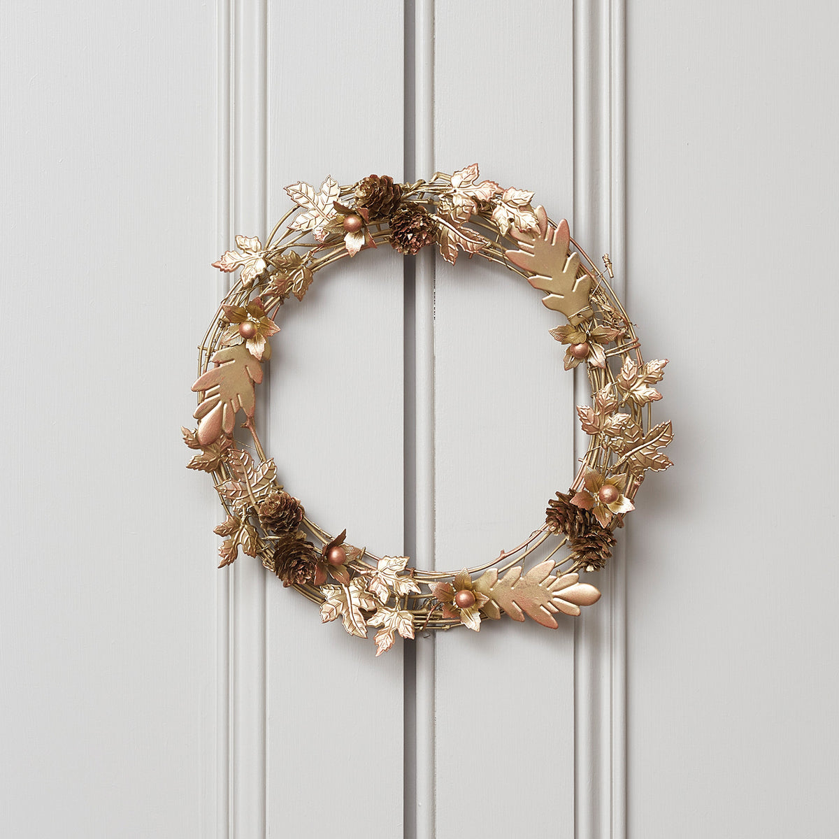 Goldener Weihnachtskranz mit Blättern und Zapfen an weißer Tür vor weißer Wand