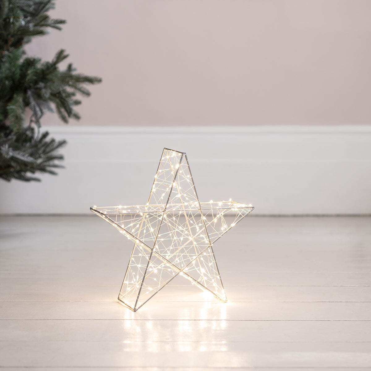 Leuchtender LED Stern mit weißen Lichtern auf hellem Boden vor Wand und Tannenzweig