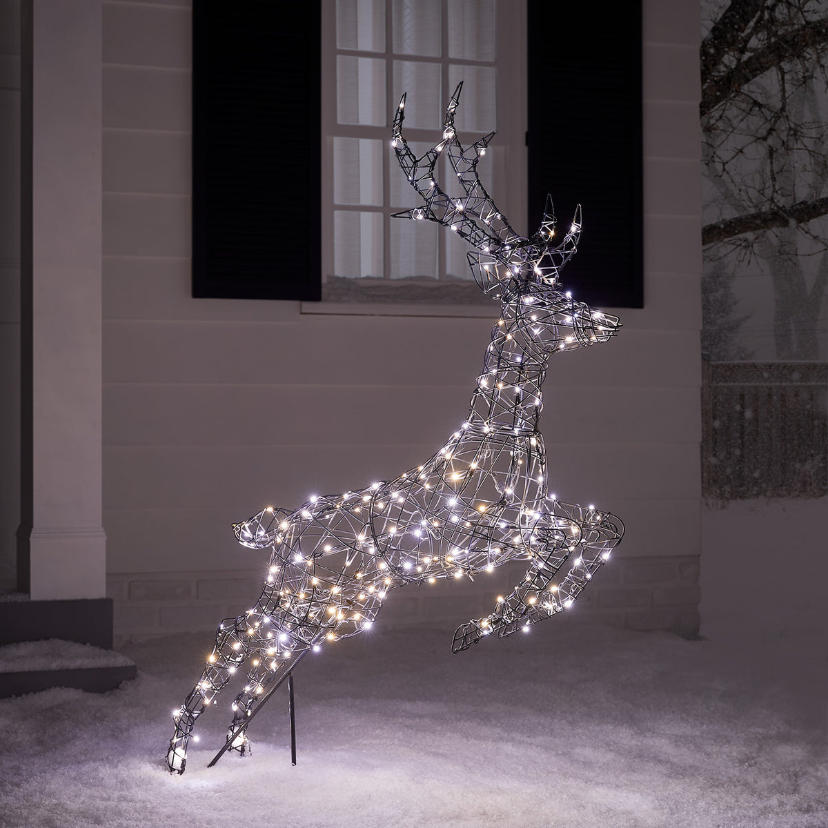 Springendes LED-Rentier mit kühlen weißen Lichtern vor Hausfassade im Schnee