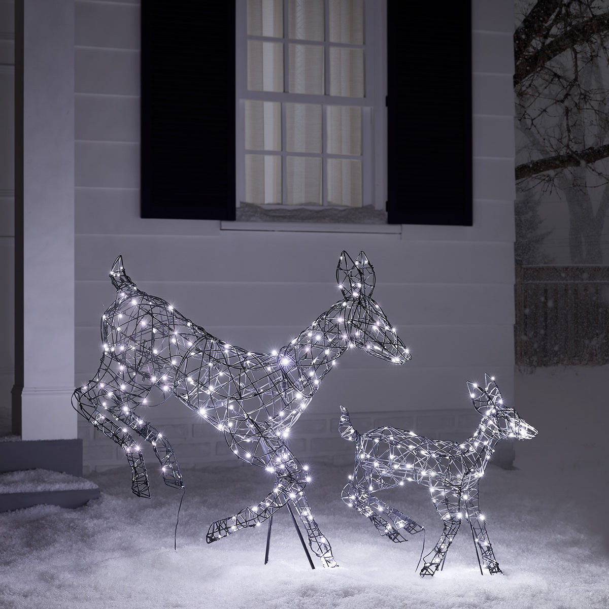 Zwei springende LED-Rentiere mit weißen Lichtern im Schnee vor einem Haus