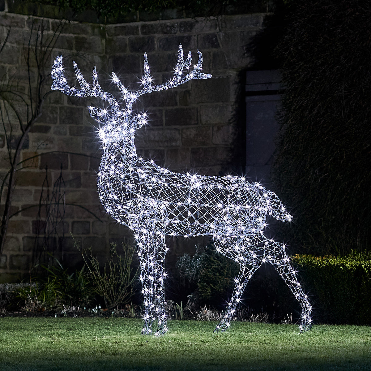 Große LED Rentierfigur mit kaltweiß leuchtenden Lichtern aus Rattanoptik im Garten bei Nacht