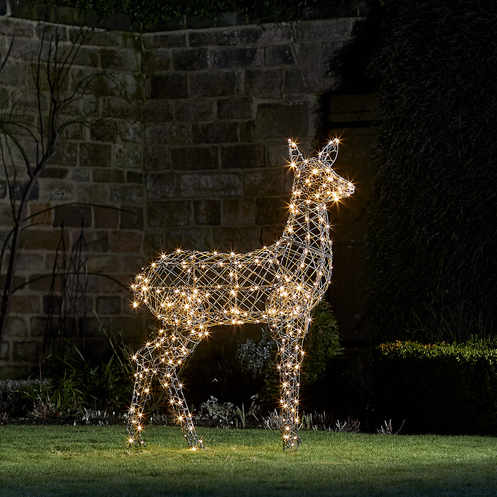 LED-Rentier Hirschkuh in grauer Rattanoptik mit warmweiß leuchtenden LEDs im Garten bei Nacht