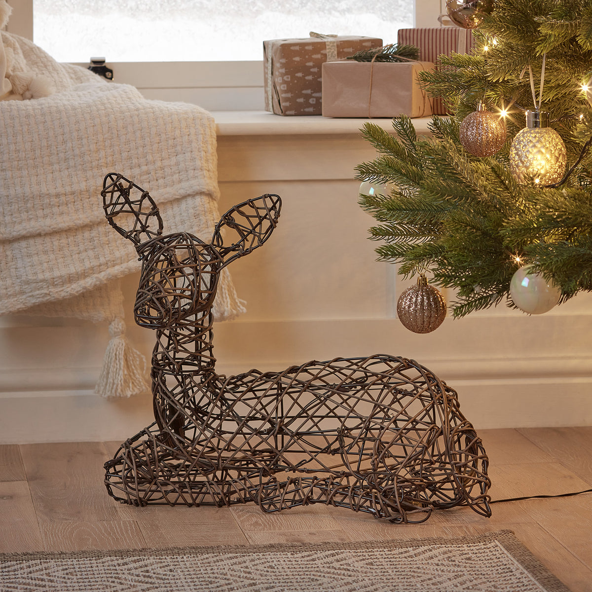 Liegendes LED-Rentier Rehkitz aus Rattanoptik vor Fenster mit Weihnachtsdeko